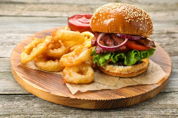 Tasty burger, fried onion rings and sauce on wooden table, closeup. Fast food