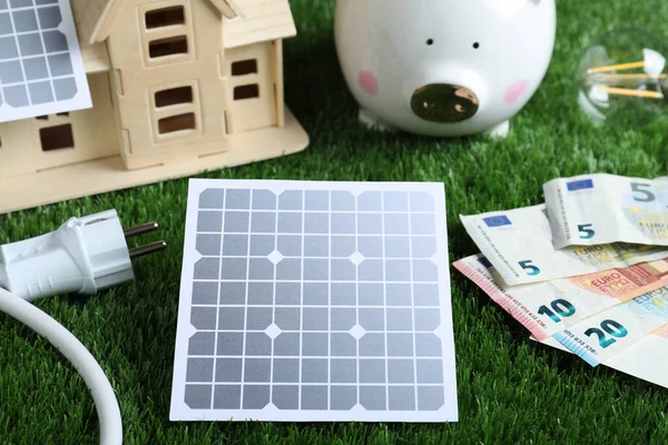 Solar panels, house model and money on green grass, closeup