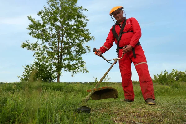 Worker cutting grass with string trimmer outdoors