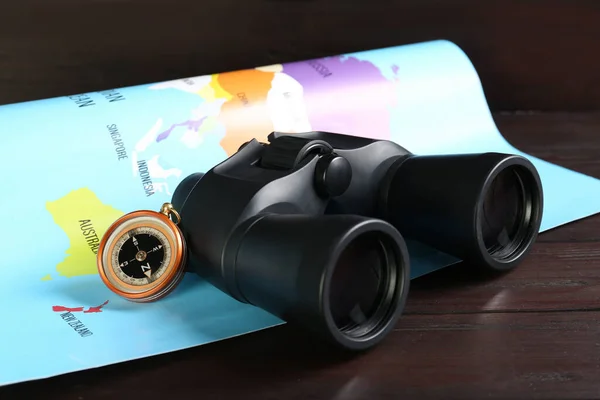 Modern binoculars, compass and map on wooden table, closeup