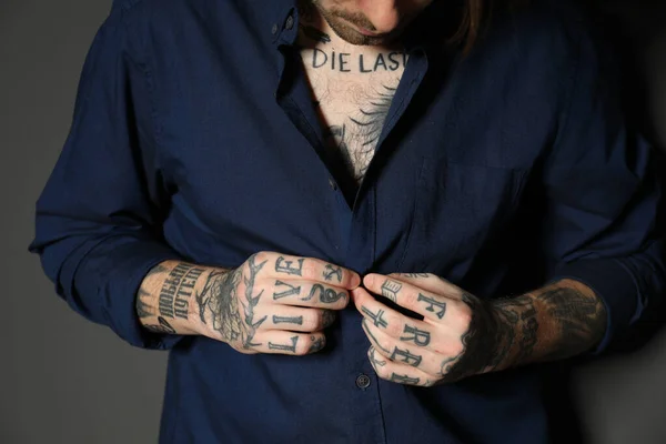 Young man with tattoos on body against black background, closeup
