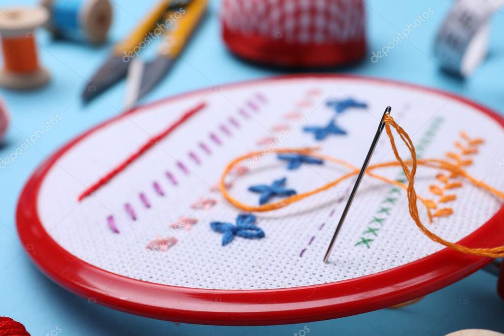 Embroidery hoop with fabric and needle on light blue background, closeup