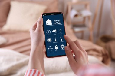 Smart Home uygulamasını kapalı mekanda cep telefonunda kullanan bir kadın.