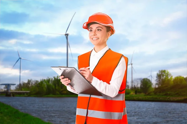 Industrial engineer in uniform and view of riverside and wind energy turbines on sunny day