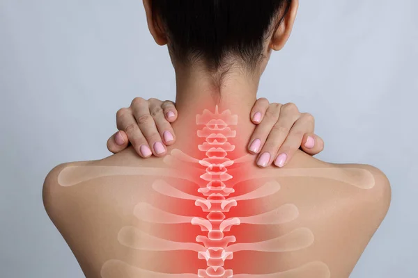 Woman suffering from pain in neck on light grey background, closeup