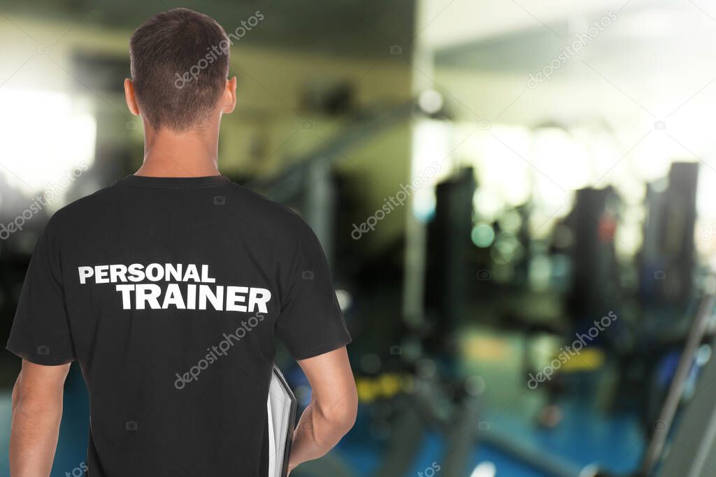Professional personal trainer with clipboard in gym. Space for text