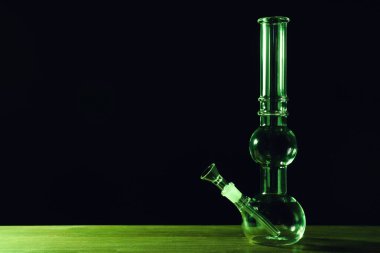 Siyah arka plana karşı ahşap masada cam bong, metin için yer. Sigara içme aygıtı