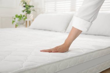 Woman touching soft white mattress on bed indoors, closeup clipart