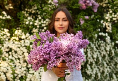 Attractive young woman with lilac flowers outdoors, focus on bunch
