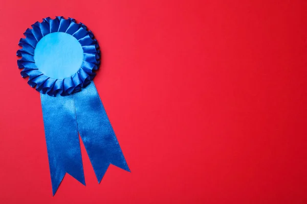 Blue award ribbon on red background, top view. Space for text