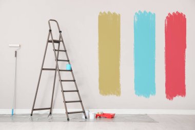 Dekoratör aletleri ve beyaz duvarın yanındaki merdiven içinde farklı boya örnekleri var.