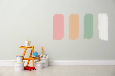 Decorator's kit of tools near white wall with samples of different paints indoors