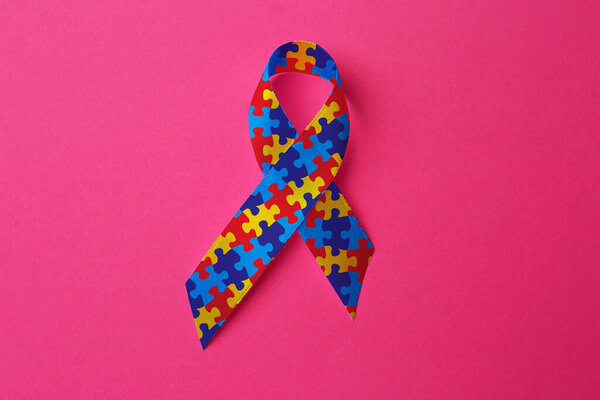 World Autism Awareness Day. Colorful puzzle ribbon on pink background, top view