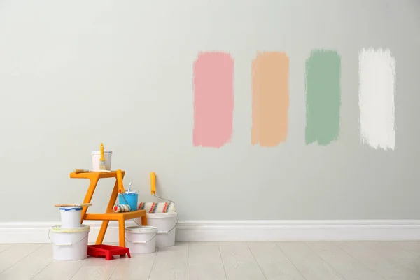 Decorator's kit of tools near white wall with samples of different paints indoors