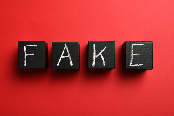 Word FAKE made with black cubes on red background, flat lay