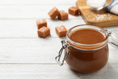 Cam kavanozda lezzetli tuzlu karamel ve beyaz ahşap masada şekerleme, metin için yer