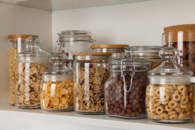 Glass containers with different breakfast cereals on shelf