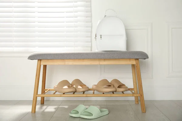 Stylish rubber slippers and storage bench with shoes in room