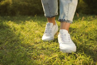 Woman in jeans and white shoes walking on green grass, closeup. Space for text