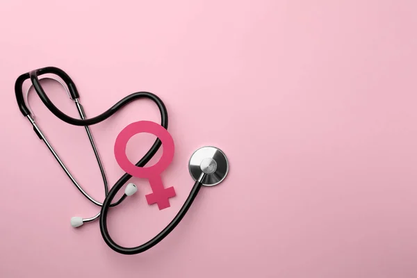 Female gender sign and stethoscope on pink background, flat lay. Space for text