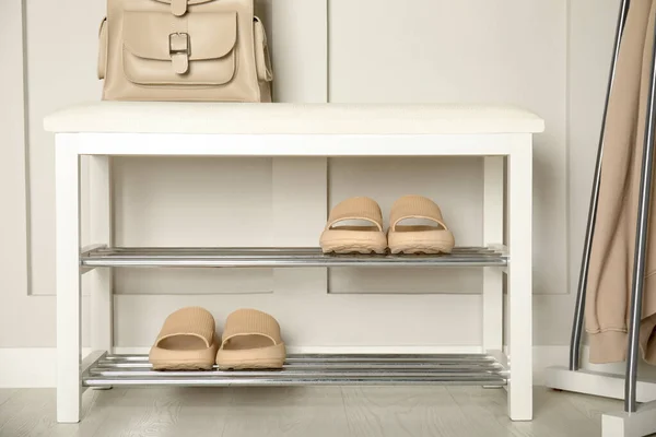 Storage bench with pairs of rubber slippers near white wall in room