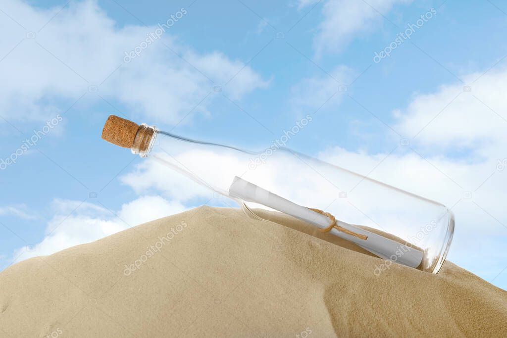 Corked glass bottle with rolled paper note on sand against sky