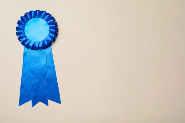 Blue award ribbon on beige background, top view. Space for text