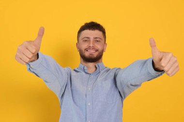 Turuncu arka planda baş parmak gösteren genç adam.