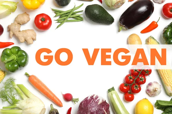 Phrase Go Vegan and fresh vegetables on white background, flat lay