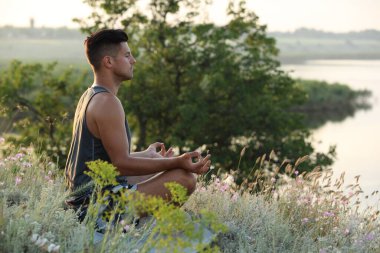 Nehir kenarındaki çayırda meditasyon yapan bir adam. Metin için boşluk