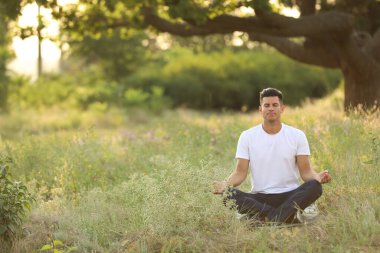 Parkta yeşil çimenler üzerinde meditasyon yapan adam, metin için alan