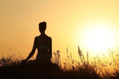 Gün batımında dışarıda meditasyon yapan bir kadın silueti. Metin için boşluk