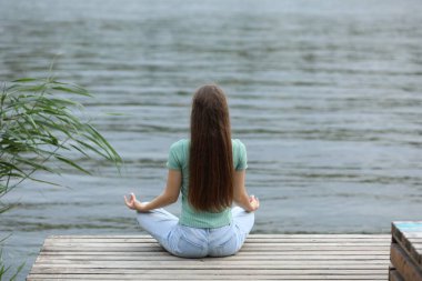 Genç bir kız nehrin kenarında meditasyon yapıyor.