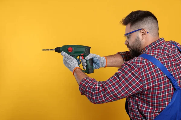 Young worker in uniform with power drill on yellow background. Space for text