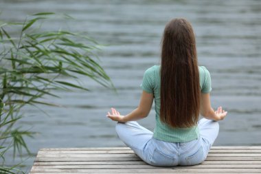 Genç bir kız nehrin kenarında meditasyon yapıyor.