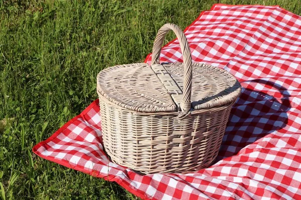 Picnic basket with checkered tablecloth on green grass outdoors