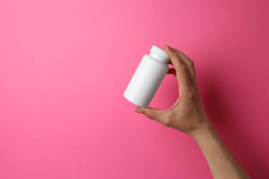 Woman holding bottle of pills on pink background, closeup. Space for text