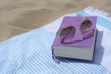 Kitap ve güneş gözlüklü plaj havlusu, mesaj için yer.