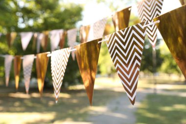 Golden bunting flags in park. Party decor clipart