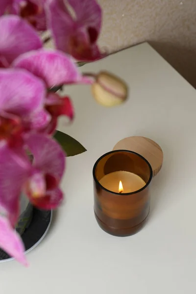 Burning Candle Glass Container Blooming Orchid White Table — стоковое фото