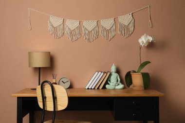 Saksı orkidesi, dekor elementleri ve kahverengi duvarın yanındaki ahşap masa üzerinde şık bir makrome.