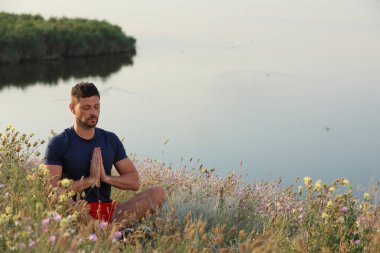 Nehir kenarındaki çayırda meditasyon yapan bir adam. Metin için boşluk