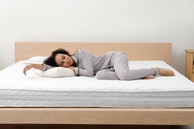 Young African American woman sleeping on bed with comfortable mattress and pillow at home