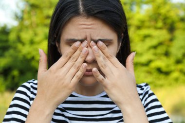 Young woman suffering from eyestrain outdoors on sunny day