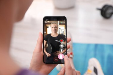 Woman having workout with personal trainer via smartphone at home, closeup