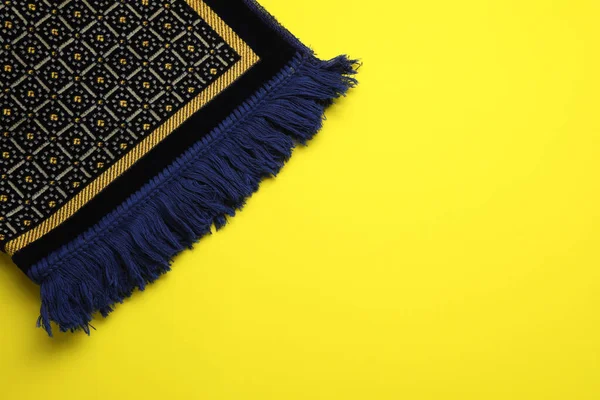 Muslim prayer rug on yellow background, top view. Space for text