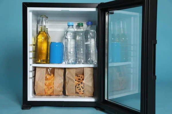 Mini bar filled with food and drinks on turquoise background, closeup