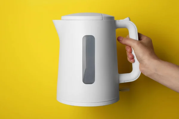 Woman holding modern electric kettle on yellow background, closeup