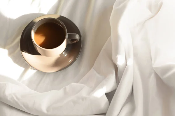 Cup of aromatic coffee on bed in morning, above view. Space for text