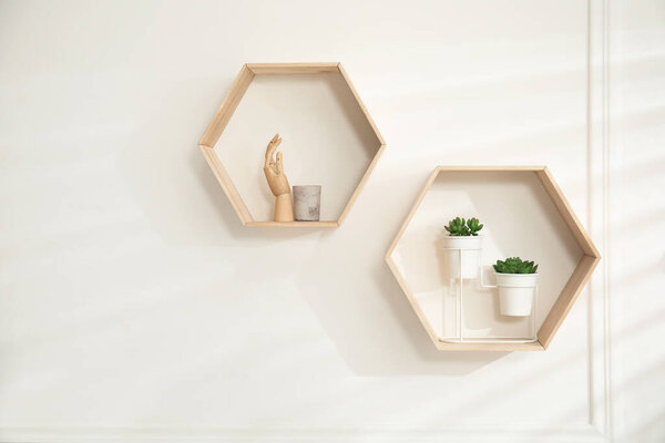 Honeycomb shaped shelves with decorative elements and houseplants on white wall